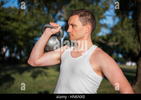 Primo piano di montare l'uomo muscolare il sollevamento di un carico pesante kettlebell nel parco all'aperto Foto Stock