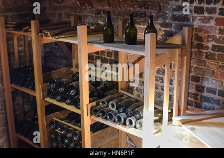 Rustico vecchie bottiglie di vino nella cantina scaffalature di legno contro un muro di mattoni Foto Stock