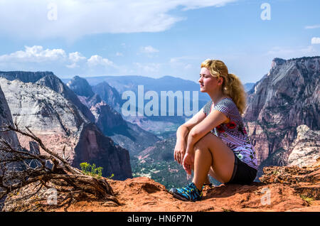 Giovane donna seduta sul bordo sulla parte superiore del canyon sul punto di osservazione trail nel Parco Nazionale di Zion Foto Stock