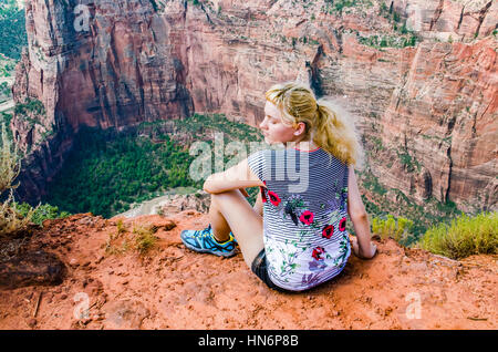 Giovane donna seduta sul bordo sulla parte superiore del canyon sul punto di osservazione trail nel Parco Nazionale di Zion Foto Stock