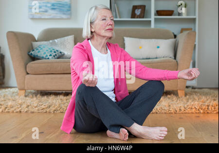 Senior donna meditando nel comfort della propria casa. Foto Stock