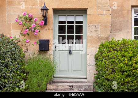 Luce verde di porte in legno in un tradizionale vecchio tiglio inglese cottage in pietra circondato da arrampicata rose rosa, lavanda, sul giorno di estate Foto Stock