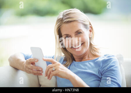 Ritratto di sorridente donna senior utilizzando il telefono cellulare nel salotto di casa Foto Stock