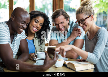 Gruppo di amici utilizzando mobile pur avendo tazza di caffè in cafÃƒÂ© Foto Stock