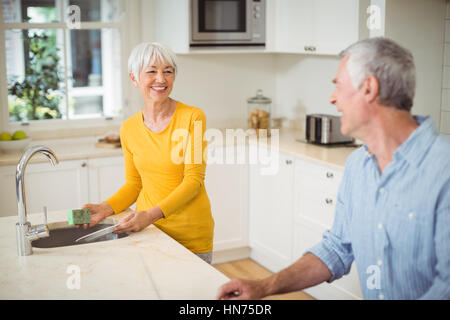 Felice donna senior di interagire con uomo in cucina mentre piatti di lavaggio Foto Stock