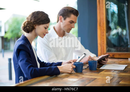 Imprenditore e la donna utilizzando il telefono cellulare e la tavoletta digitale al contatore in cafe Foto Stock