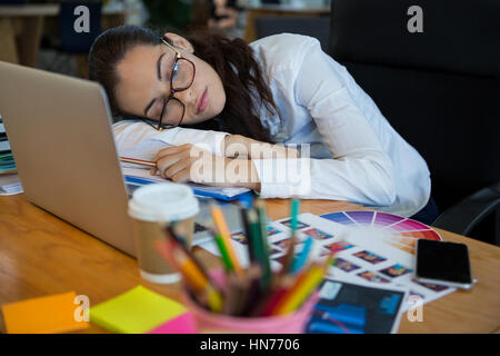 Stanco di sesso femminile graphic designer a dormire la scrivania in ufficio Foto Stock