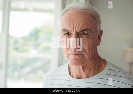 Ritratto di pensosa senior uomo in piedi accanto alla finestra a casa Foto Stock