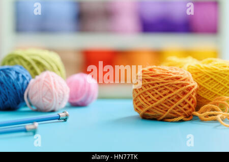 Filati per maglieria e aghi sul tavolo blu contro sfondo sfocato. Close up multi colore palle di lana. Foto Stock