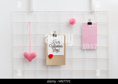 Buon San Valentino scheda su una griglia metallica visualizzare con maglia cuore rosa e pom pom. Il giorno di San Valentino la decorazione. Griglia di parete organizzatore. Foto Stock