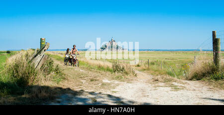 Francia, MONT SAINT MICHEL - Agosto 10 2012: Panorama dell'isola con campo verde e un paio di turisti durante le vacanze in bicicletta Foto Stock
