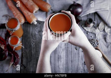 Ferro da stiro la tazza con il succo di carota in mani femminili, vista dall'alto, tonificazione vintage Foto Stock