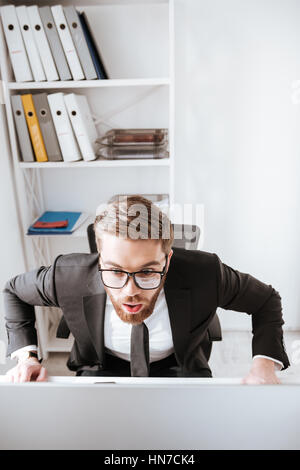 Foto di scioccato imprenditore barbuto seduto in ufficio mentre guardare il computer Foto Stock