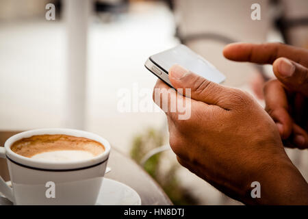 Tagliate vista colpo di una mano di un uomo utilizzando smart phone mentre sedendo nel cafè sul marciapiede in giorno di estate Foto Stock