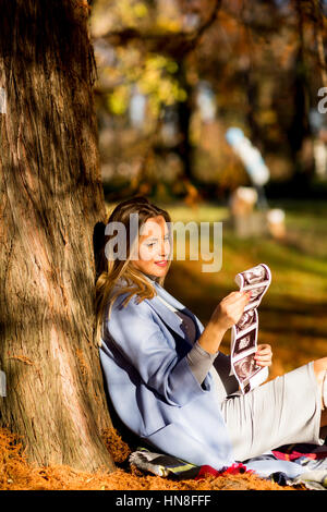 Giovane donna incinta seduta in autunno park e guardando atultrasounds foto di baby Foto Stock