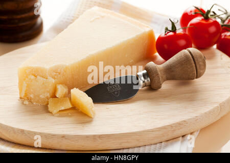 Il Grana Padano formaggi e il coltello con il logo sul piatto di legno, pomodori e pepe mulino in background. Il Grana Padano è un disco chee Foto Stock