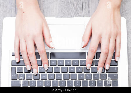 Vista ravvicinata delle mani di una giovane donna digitando su una tastiera portatile preso dalla testa Foto Stock