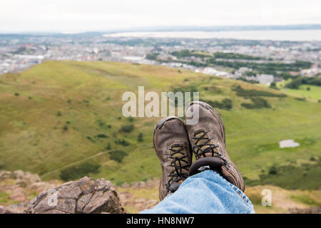 Regno Unito, Scozia, Edimburgo - un maschio del turista scarpe seduto in cima Arthur' Seat, il picco principale del gruppo di montagne guardando sopra la città di Foto Stock