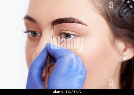 Raccolto di estetista in guanti blu applicando speciale trucco permanente delle sopracciglia per brunette donna. Professional rendendo sopracciglia permanente utilizzando p Foto Stock