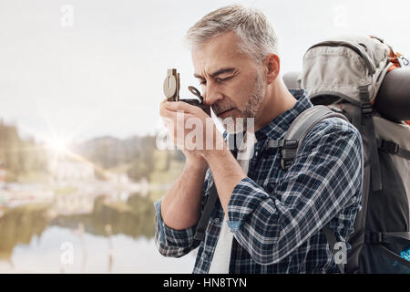 Escursionista trekking sulle montagne ed esplorando la natura, egli è utilizzando un escursionismo bussola e direzioni di ricerca Foto Stock