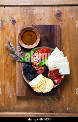 Snack su una piastra di argilla e lo sfondo di legno. stile rurale. prosciutto, formaggio, prugne, mele, noci Foto Stock