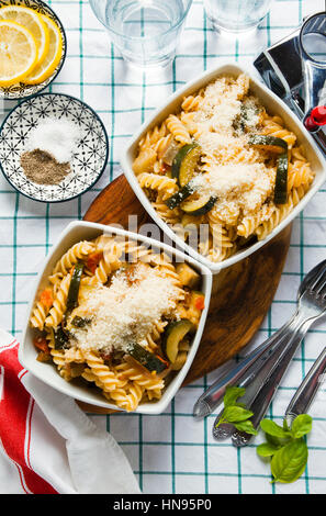 Hot insalata di pasta con zucchine zucchine e parmigiano. su bianco tovaglia a scacchi. Grattuggia formaggio. Foto Stock