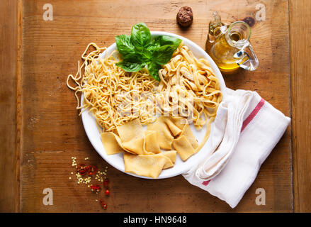 Vari tipi di fatti in casa la Pasta fresca sulla piastra su un sfondo di legno Foto Stock