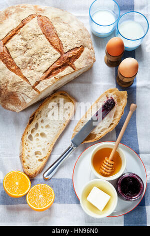Tavolo per la colazione. Pane, uova sode, burro, miele, marmellata, arance, latte Foto Stock