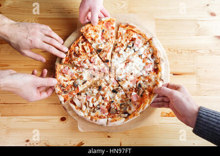 Close-up di persone tenendo le mani delle fette di pizza. su una superficie di legno Foto Stock