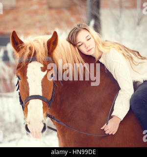 Pilota giovane ragazza con i capelli lunghi che giace sul collo del cavallo. Friensdhip sfondo. Calda tonalità di colore immagine Foto Stock