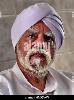 Un anziano Sikh indiano con una barba bianca e sopracciglia folta e con un abbigliamento bianco e un turbante bianco. Foto Stock