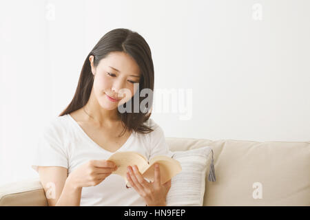 Giovane donna giapponese sul divano in una camera bianca Foto Stock