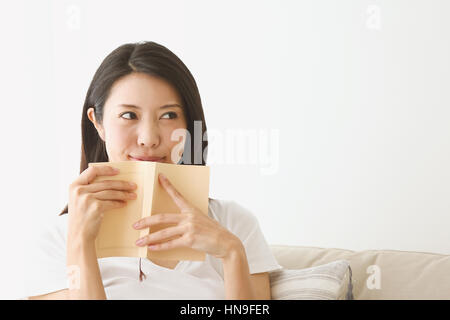Giovane donna giapponese sul divano in una camera bianca Foto Stock