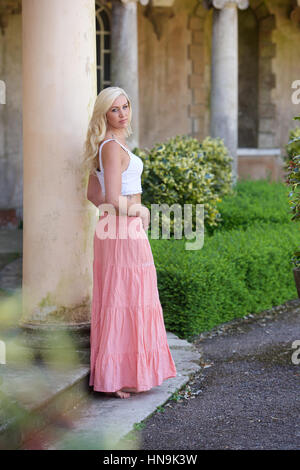 Bella giovane donna in lungo mantello di colore rosa e bianco superiore all'aperto Foto Stock