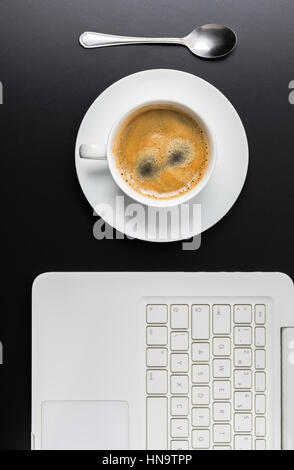 White tazza di caffè su sfondo scuro con il computer portatile. Vista dall'alto. Foto Stock