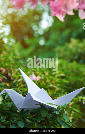 White paper origami gru su erba verde e sfocata sullo sfondo del giardino Foto Stock
