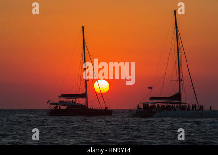 Tramonto sul mare Mediterraneo visitati dai turisti di un catamarano a Baia di Ammoudi, Oia - Santorini, un'isola greca delle Cicladi gruppo Foto Stock