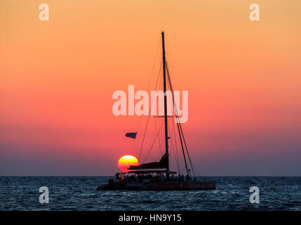 Tramonto sul mare Mediterraneo visitati dai turisti di un catamarano a Baia di Ammoudi, Oia - Santorini, un'isola greca delle Cicladi gruppo Foto Stock