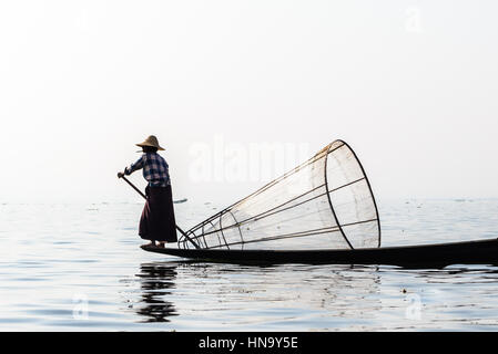 Pescatore birmano sulla barca di bambù per la cattura di pesce in modo tradizionale con la rete a mano. Lago Inle, Myanmar (Birmania) destinazione di viaggio Foto Stock