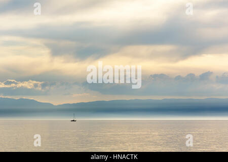 Silhouette di barche a vela sulle acque del lago di Ginevra in un giorno di nebbia nella luce del sole che lentamente si sta avvicinando l'orizzonte è visto nel di Foto Stock