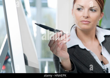 Junge Geschaeftsfrau zeigt mit Stift auf Monitor - young business woman punti al monitor Foto Stock