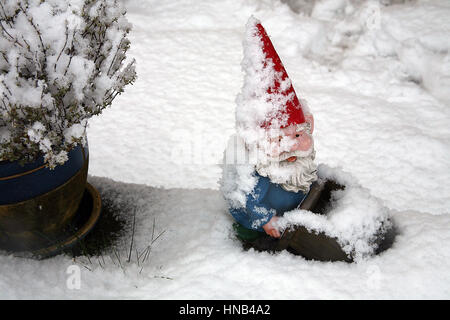 Coperta di neve gnomo da giardino in rosso cappello appuntito Foto Stock