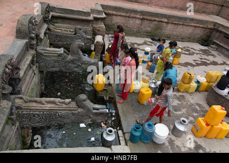 La gente in coda per acqua che proviene da sorgenti sotterranee dalle intricate sculture di bronzo beccucci in una piazza di Kathmandu, Nepal Foto Stock