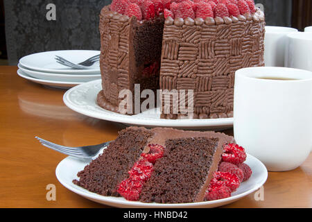 Fetta di fatto in casa di design originale torta al cioccolato con lamponi freschi e il riempimento di lamponi e servite su un piatto con tutta la torta nel backgro Foto Stock