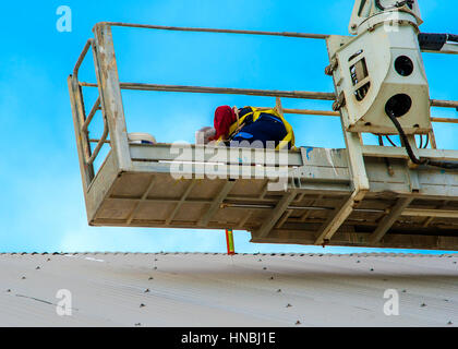 Le riparazioni del lavoratore coperchio di metallo su un piccolo cestino passeggero camion gru Foto Stock