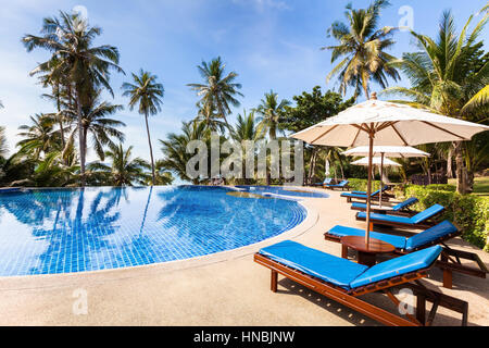 Bella spiaggia tropicale front hotel resort con piscina, lettini e palme durante un giorno caldo e soleggiato, destinazione paradiso per le vacanze Foto Stock