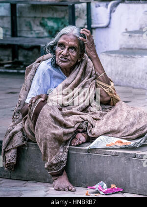 Madurai, India - 19 Ottobre 2013: un vecchio ingrigimento lady si siede sul marciapiede della strada intorno al Tempio di Madurai. Ella ha un espressivo licenziamento fa Foto Stock