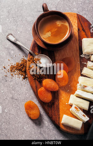 Turrón affettato su una tavola di legno con albicocche secche, fichi secchi e una tazza di caffè. snack sani, super cibo Foto Stock