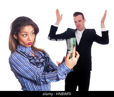 Giovane donna aziendale rende selfie con il cellulare mentre man in black suit non guarda divertito Foto Stock