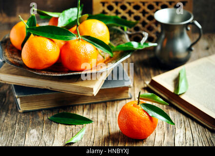 Tangerini freschi e libri su un tavolo di legno Foto Stock